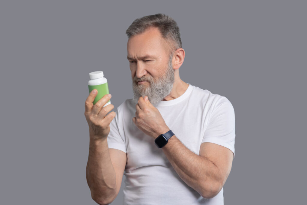 A bearded man holding a jar with vitamins